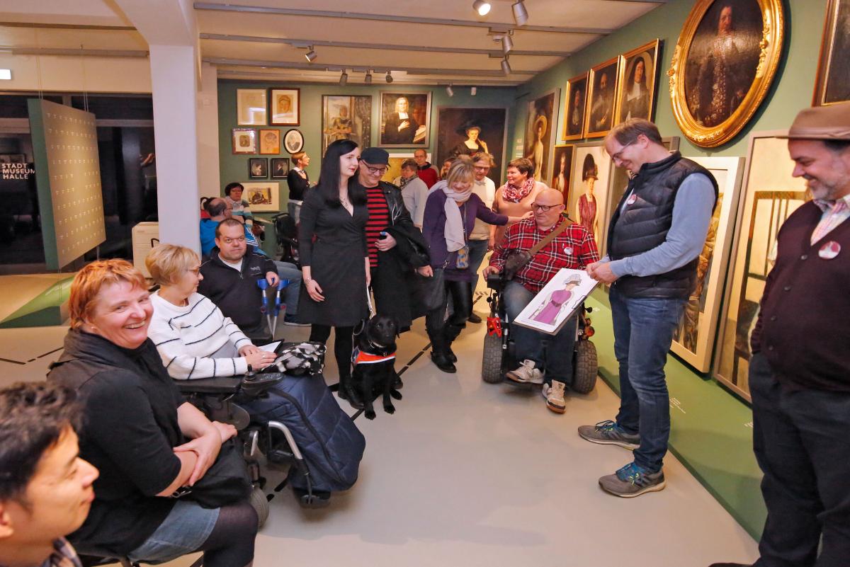 Eine Gruppe von Menschen, sitzend und stehend gegenüber der Portraitgalerie. Gero Sievers zeigt ein tastbares Bild.