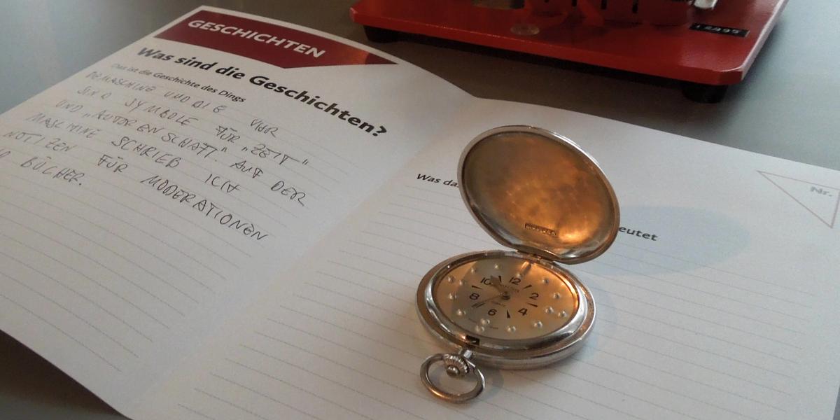 Eine aufgeklappte silberne Taschenuhr mit tastbaren Zeigern auf einem Objektformular.
