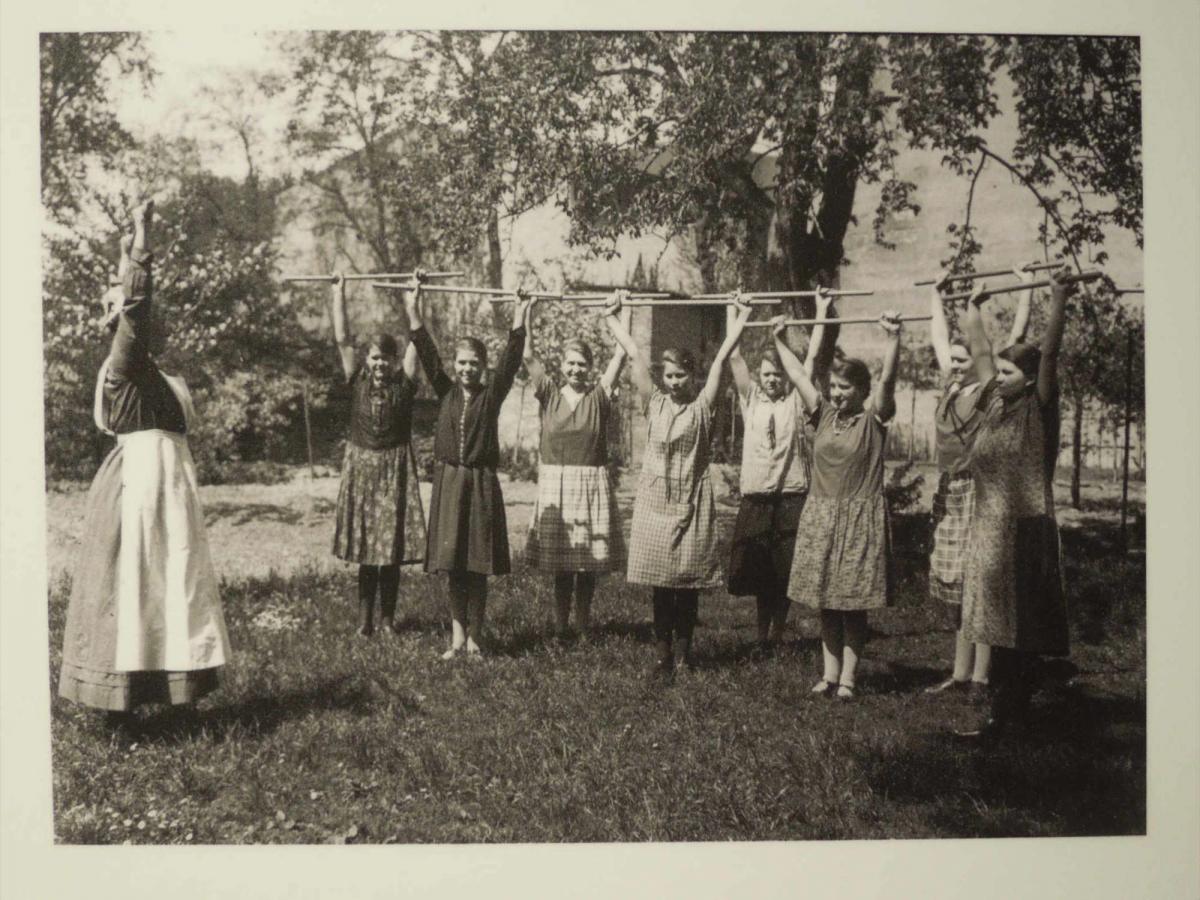 Eine Gruppe junger Mädchen in Kleidern bei Gymnastikübungen im Freien