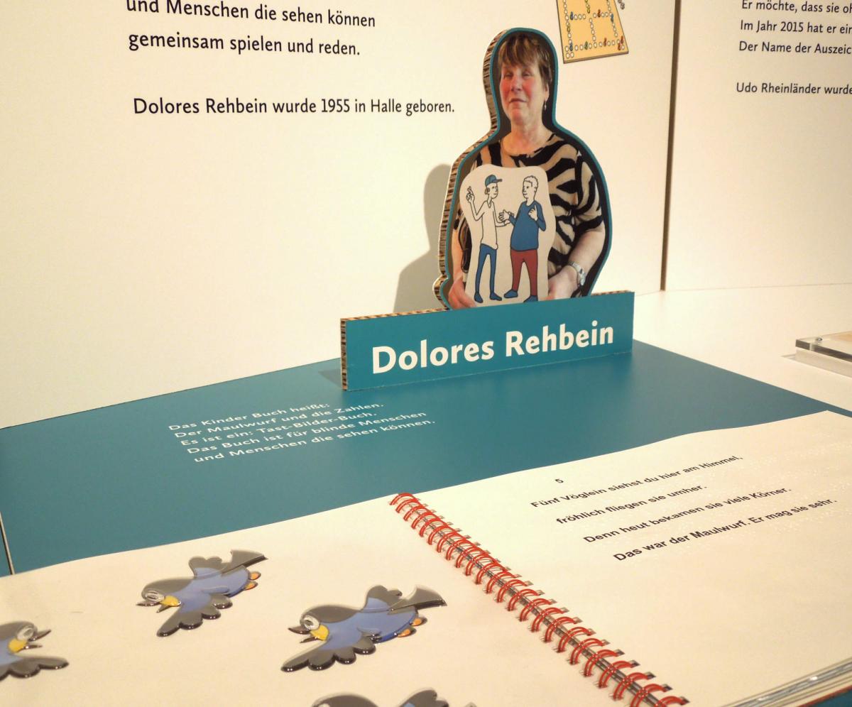 Detail Ausstellungstisch mit aufgeschlagenem Tastbilderbuch und Foto von Dolores Rehbein