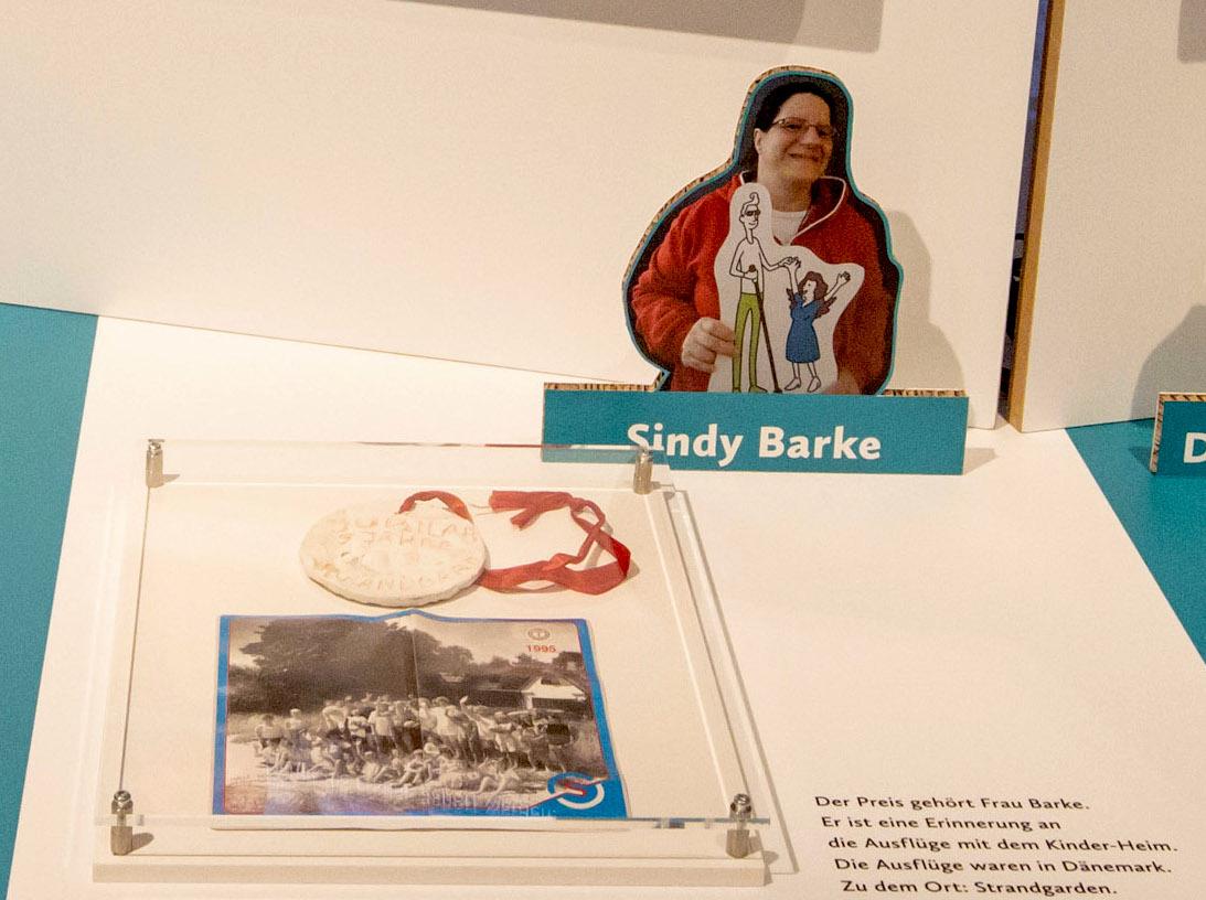 Detail Ausstellungstisch mit Gipsmedaille und Gruppenfoto unter einer Acrylplatte sowie dahinter ein Foto von Sindy Barke