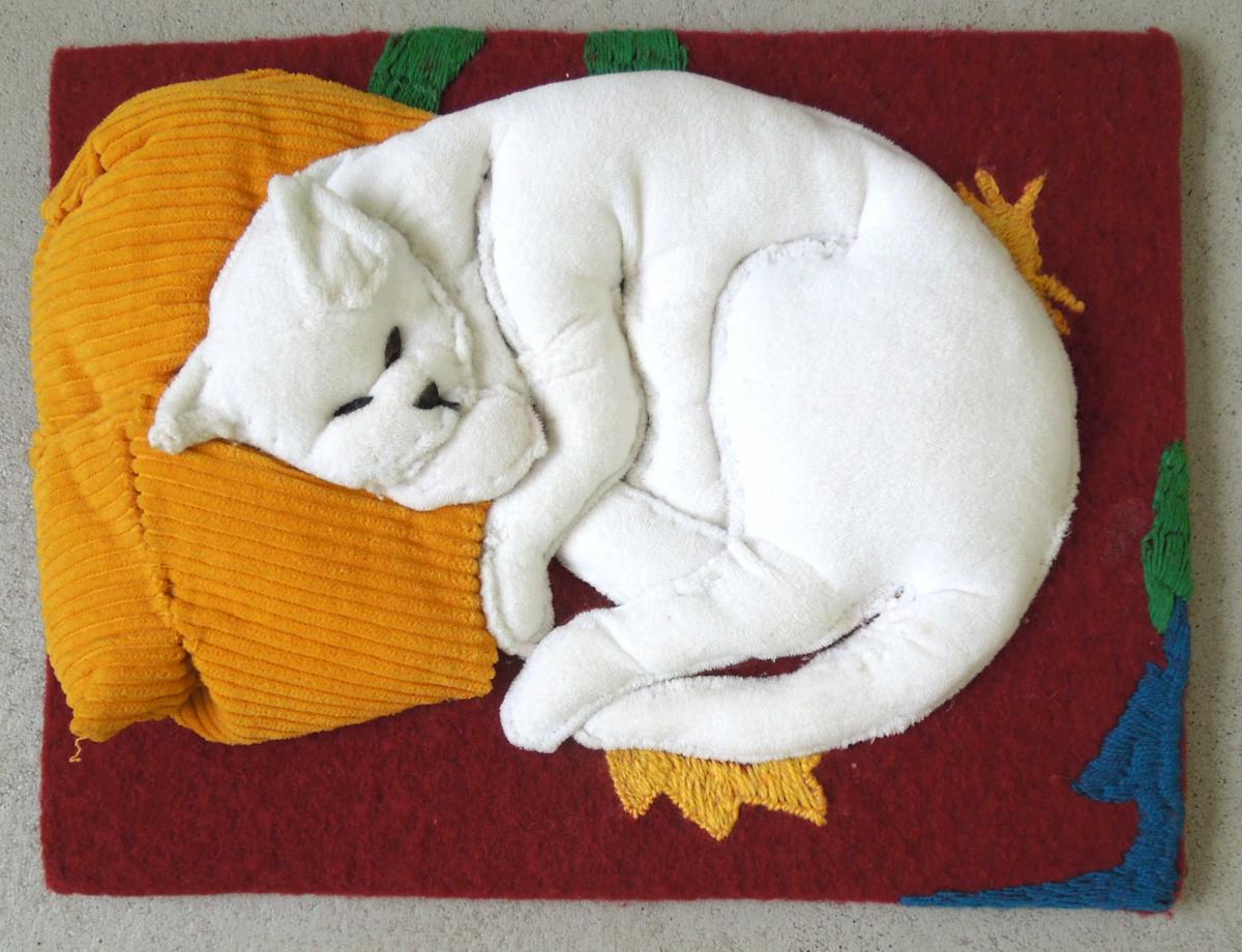 Tastobjekt aus verschiedenen, teilweise unterfütterten Stoffen nach dem Gemälde "Die weiße Katze". Eine Katze liegt leicht zusammengerollt auf einer roten Decke und einem gelben Kissen. 