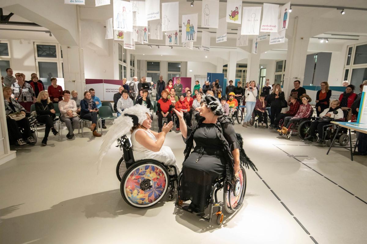 zwei Frauen in Engelskostümen beim Rollstuhltanz vor Publikum